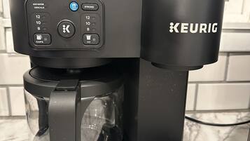 A black Keurig coffee maker with a glass carafe and a water reservoir, placed on a marble countertop.