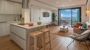 Una cocina moderna con una isla central, un área de comedor con vistas al océano y una sala de estar con sofá y sillones.