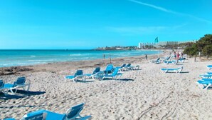 Une plage bordée de rangées de chaises longues bleues, avec un hôtel en arrière-plan.