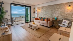 Un salón moderno con un gran ventanal corredero que da a un balcón con vistas al mar.