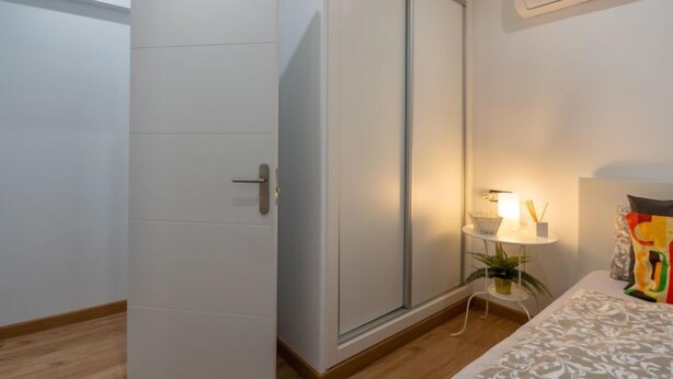 Une chambre à coucher avec un lit, une table de chevet avec une lampe, une plante en pot et une porte coulissante.