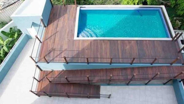 A rectangular swimming pool with a wooden deck and a white tiled floor. - Elevated Experience at the Bromptons (Kingston)