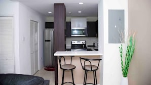 A compact kitchen with a refrigerator, microwave, stove, and two bar stools. - Elevated Experience at the Bromptons (Kingston)
