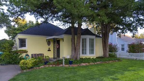 Uma casa amarela com telhado escuro, cercada por um gramado bem cuidado e uma cerca branca de piquete.