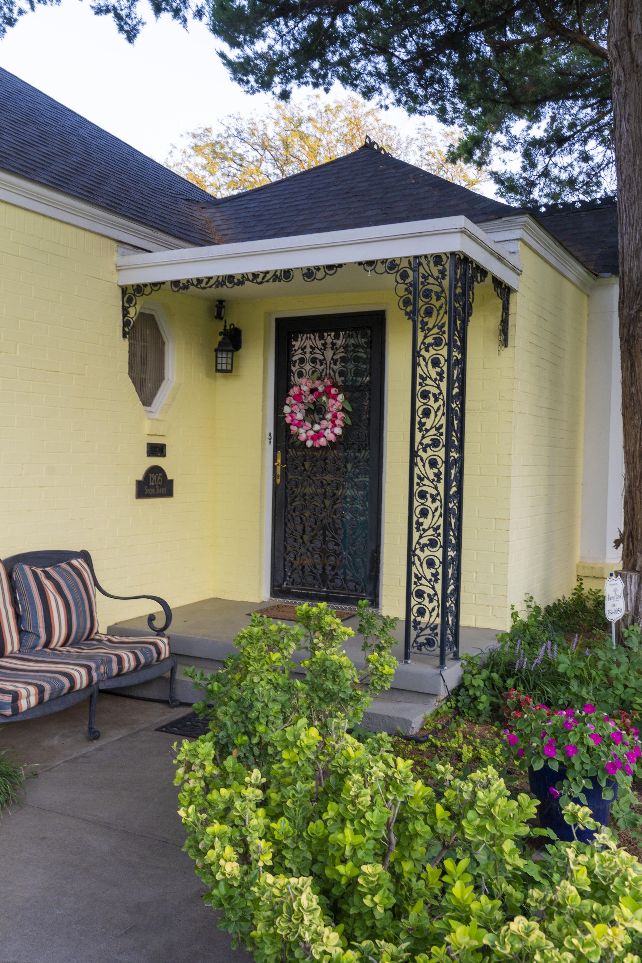 A yellow house with a black door, a porch with a bench, and a wreath on the door.