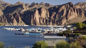 Un puerto deportivo con barcos amarrados, un puente al fondo y montañas.