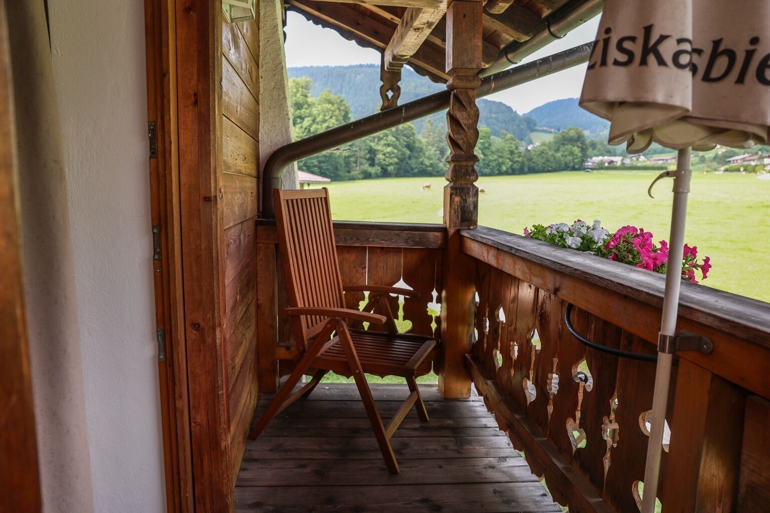 A wooden porch with a chair and a view of a green landscape.