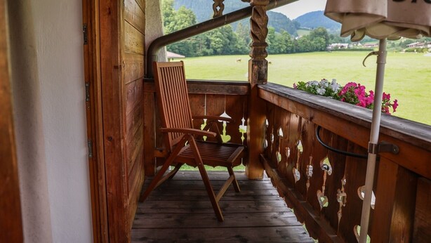 Een houten veranda met een stoel en uitzicht op een groen landschap.