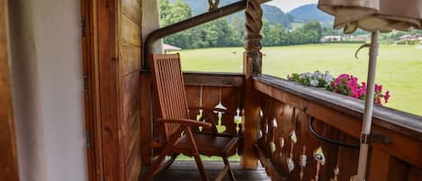 A wooden porch with a chair and a view of a green landscape.