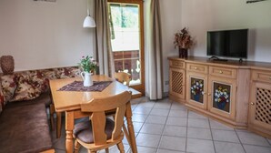 Una sala acogedora con una mesa de comedor de madera, un sofá, un televisor y un aparador con adornos florales.