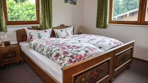 Un dormitorio con una cama de madera, ropa de cama estampada, dos mesitas de noche y un ventanal con cortinas.