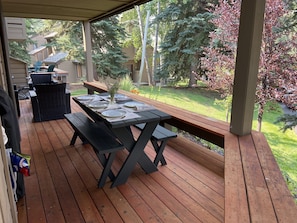 A covered patio with a wooden table set for dining, surrounded by benches and a grill area. - Sun Valley Retreat (Sun Valley)