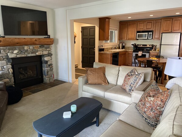 Relax in this inviting living space with a cozy fireplace, comfortable sofa, and adjacent kitchen.