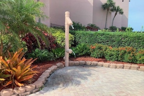 A landscaped area with a water feature, a paved walkway, and a variety of plants. - Beachfront at Siesta Breaker | 2nd Fl | Gulf Views (Sarasota)