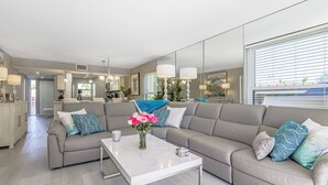 Un salon moderne avec un canapé d’angle gris, une table basse blanche et un vase rempli de fleurs roses.