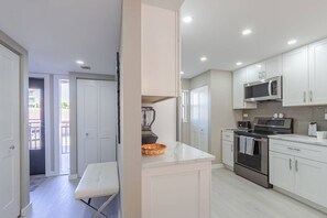 A modern kitchen with white cabinetry, a built-in oven, microwave, and a countertop with a blender. - Beachfront at Siesta Breaker | 2nd Fl | Gulf Views (Sarasota)