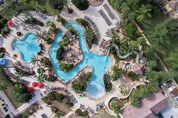 Relax by the resort's central swimming area, featuring a winding water slide and pool, surrounded by lush greenery and lounge areas.