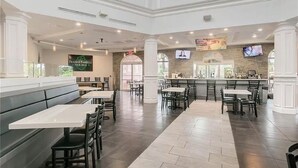 Un restaurante espacioso con techos altos, varias zonas de estar que incluyen cabinas y mesas, un bar y una pantalla de televisión en la pared.