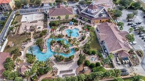 Vista aérea de un resort con múltiples piscinas, palmeras y un estacionamiento.