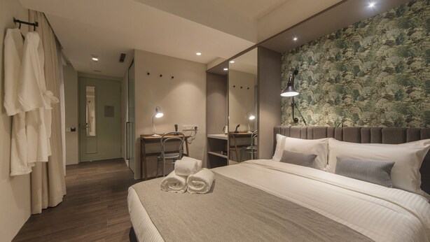Habitación de hotel con una cama grande, un escritorio, una silla, un espejo y zona de ducha.