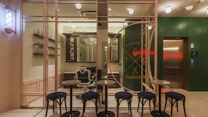 Interior de una barbería con una mampara de vidrio, varios sillones y un ascensor a la vista.