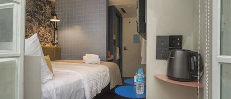 A hotel room with a bed, a small table with a water bottle, a coffee maker, and a TV on the wall.