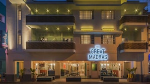 Un hotel con un cartel llamativo que dice "The Great Madras". Cuenta con varios balcones con asientos al aire libre y una entrada bien iluminada.