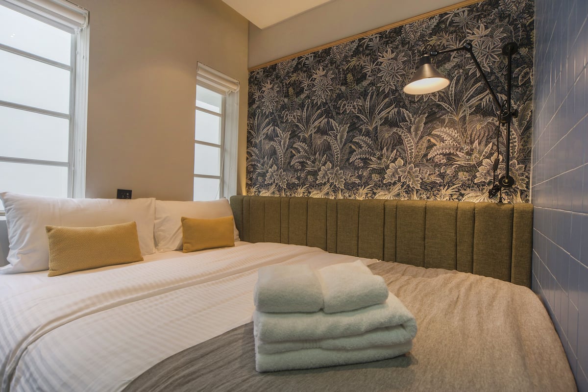 Une chambre d’hôtel avec un grand lit, une tête de lit et un mur orné d’un motif floral, ainsi qu’une lampe de chevet.