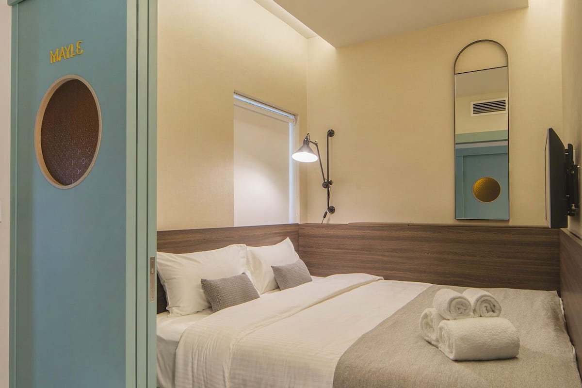 Une chambre d’hôtel avec un lit, une table de chevet, un miroir et une porte portant l’inscription « MAILE ».
