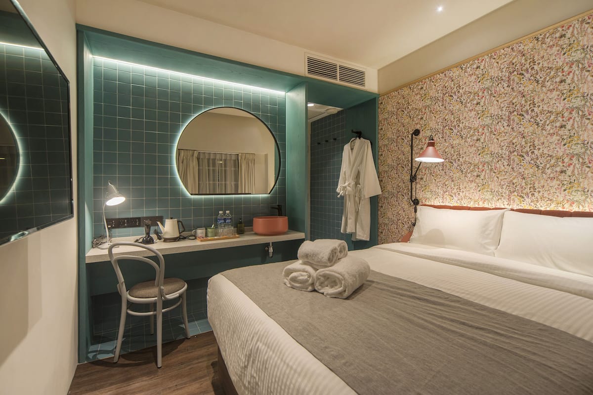 Une chambre d’hôtel comprenant un lit, un bureau avec une chaise, un miroir, un peignoir et une lampe.