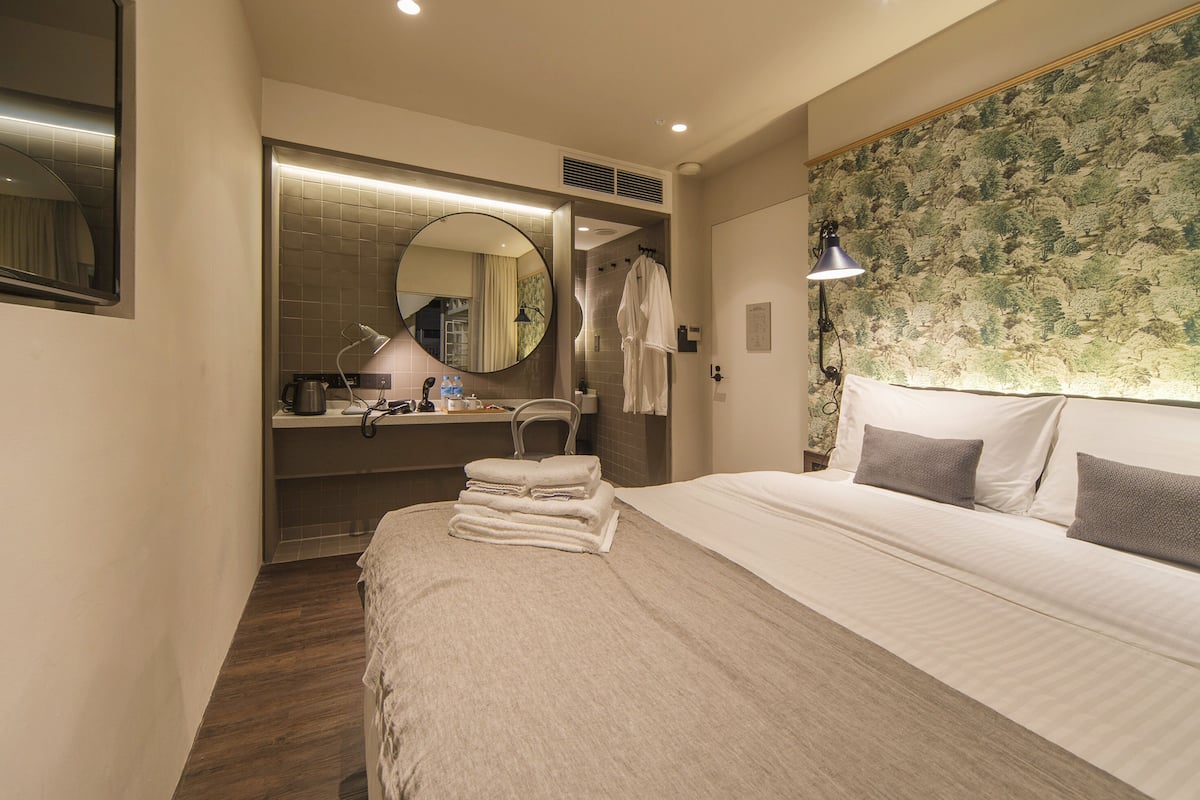 Une chambre d’hôtel avec un grand lit, un miroir rond, une coiffeuse avec un lavabo et un espace douche.