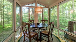 A conservatory with a round table and chairs, large windows, and a hanging light fixture.