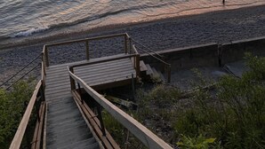 A wooden staircase leading to a beach with a view of the ocean and a sunset.