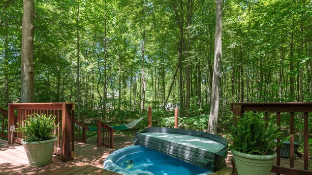 A hot tub on a wooden deck surrounded by lush greenery.
