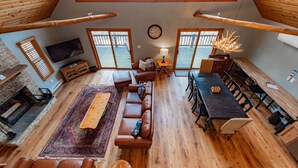 A spacious loft-style living area with a large sofa, dining table, and a fireplace. - Rustic Woodsy Getaway w/Hot Tub & Fireplace (Oakland)