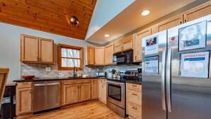 A modern kitchen with wooden cabinets, stainless steel appliances, and a brick backsplash. - Rustic Woodsy Getaway w/Hot Tub & Fireplace (Oakland)