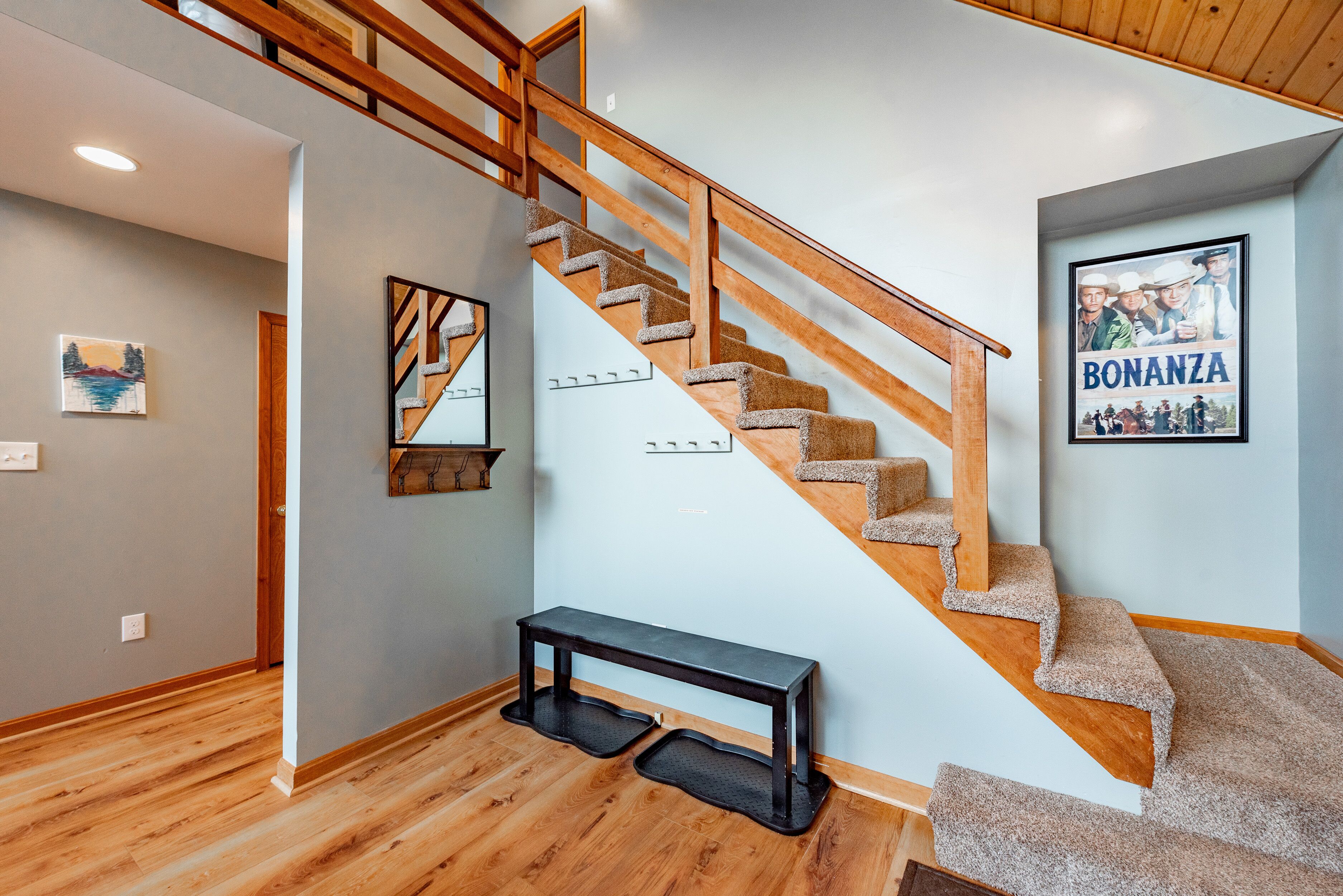 A staircase with wooden railings and carpeted steps, a bench, and a framed picture on the wall.
