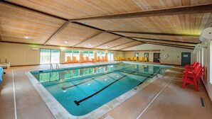 Ein Innenpool mit Holzbalken an der Decke, einem klaren Wasserbereich und orangefarbenen Stühlen entlang der Seiten.