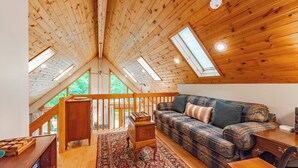 Ein gemütliches Schlafzimmer im Loft-Stil mit Holzbalkendecke, Dachfenstern, einem Karo-Sofa und einem kleinen Holztisch.