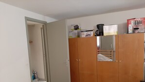 Un dormitorio con un armario, una cama con colcha estampada y una pequeña mesa cubierta con un paño amarillo.