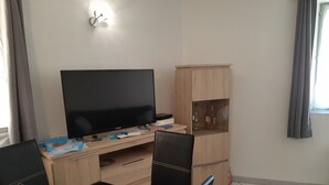 Una habitación con televisión, escritorio, silla, armario y ventana.