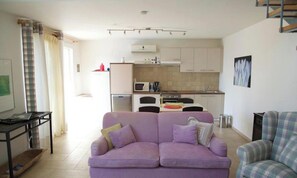 A living room with a purple sofa, a plaid armchair, a kitchen with white cabinets, and a microwave.