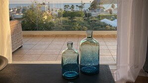 Un balcón con dos botellas de vidrio, un libro titulado "Greece La Cuisine Authentique", y vistas al mar y edificios.