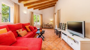 Una sala de estar con un sofá rojo, un televisor sobre un mueble blanco y piso de baldosas.