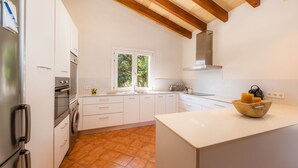 Una cocina moderna con armarios blancos, horno empotrado, lavadora y ventana con vista a follaje.