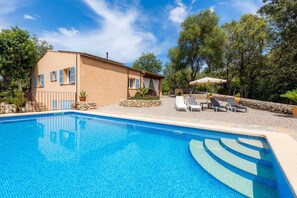 Une piscine à l’eau d’un bleu cristallin, une maison avec un toit en tuiles et un mur en pierre.