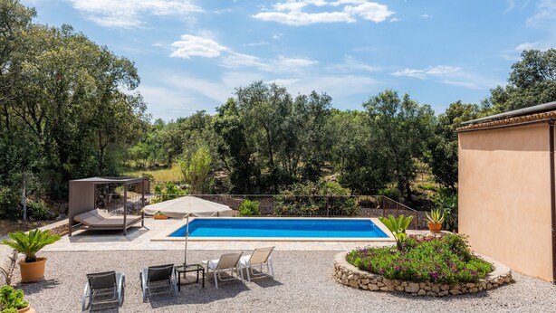 Una piscina con una pérgola, sillones de descanso y un jardín de piedra.