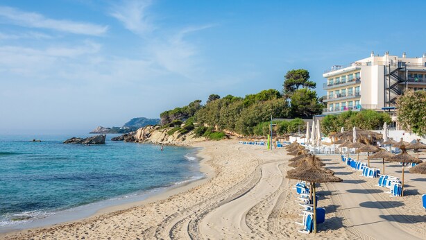 Ein Strand mit einem Gebäude, blauem Himmel und ruhiger See.