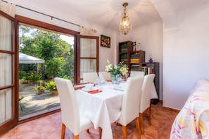 A dining area with a table set for four, surrounded by chairs, with a view of the garden through large windows.