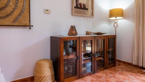 Ein Zimmer mit einem Holzkabinent, einem Wandbehang aus Gewebe, einem gerahmten Kunstwerk und einer Stehlampe.